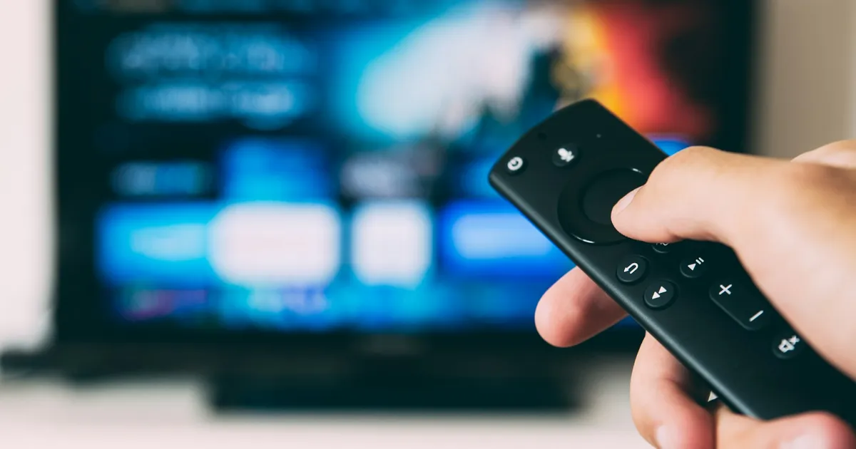 Hand pointing a streaming stick remote at a TV — ViviMate Firestick setup
