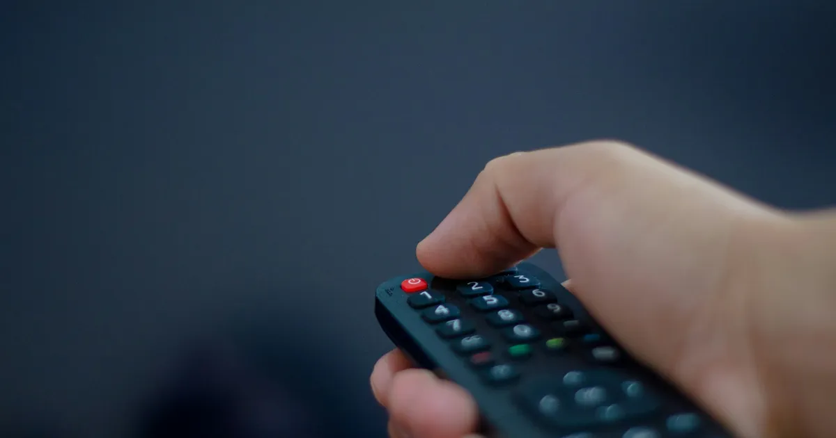 Hand holding a TV remote control — ViviMate IPTV guide