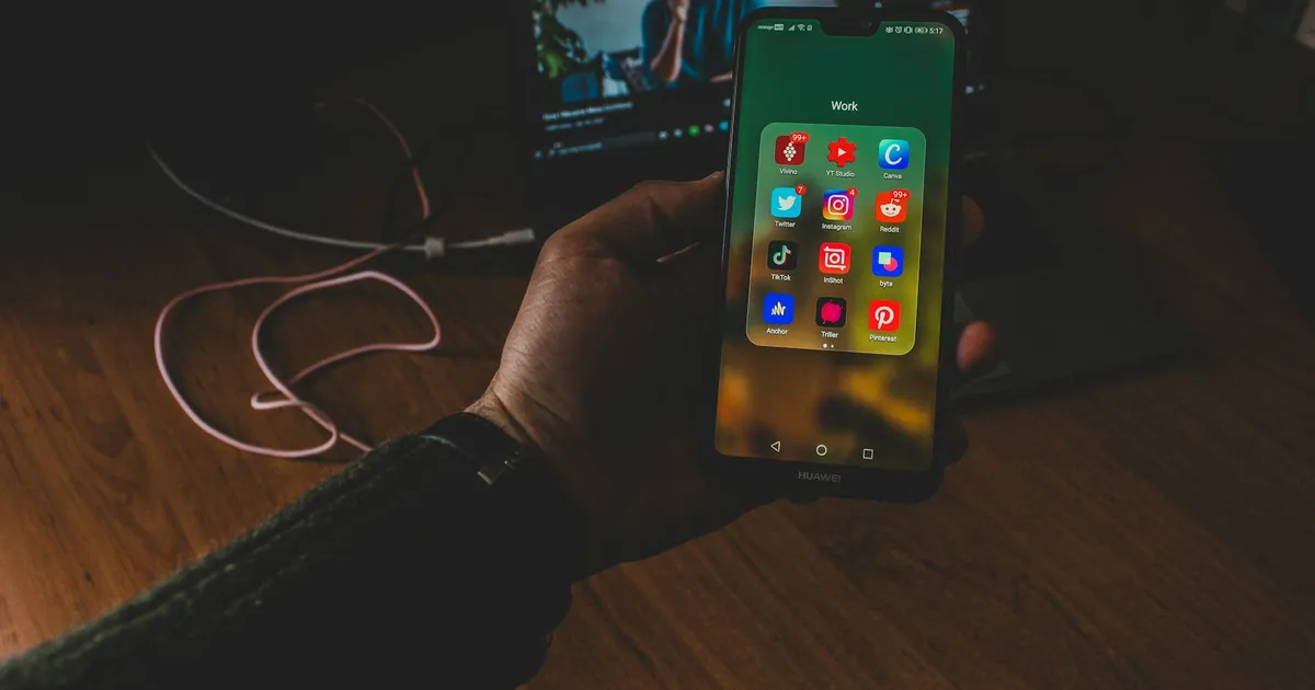 Person holding a smartphone with apps on screen in front of a laptop — choosing an IPTV player for ViviMate